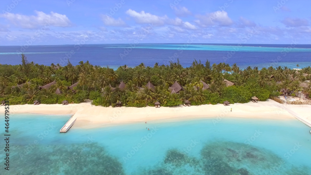 Beautiful resort island in the Maldives, bungalows among palm trees, sandy beach, blue clear water