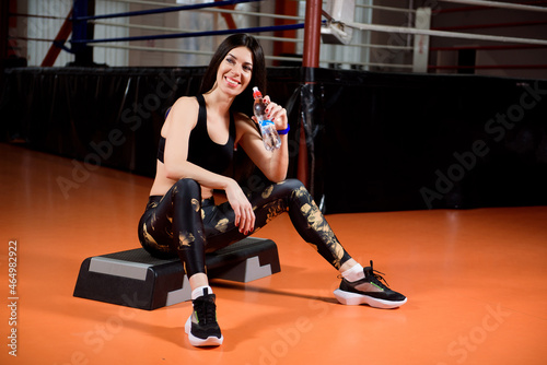 Attractive sports girl smiles and drinking water standing in fitness class.