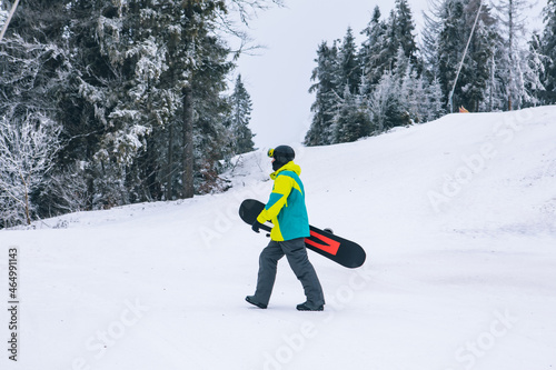 man with snowboard walking by snowed hill