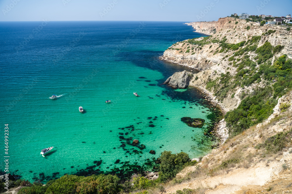 Boats and yachts in the crystal clear azure sea on a sunny day. Cape Fiolent in Sevastopol. The concept of an ideal place for summer travel and relaxation