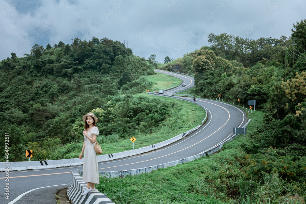 Lady walking on Road no.3 or sky road on Root 1081 over top of mountains with green jungle in Santisuk - Bo Kluea District, Nan province, Thailand.