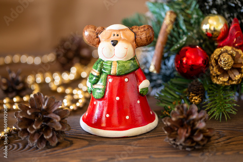 Christmas festive background with a toy deer dressed as Santa Claus, Christmas tree decorated with decor with golden lights, festive background on a wooden table, close-up