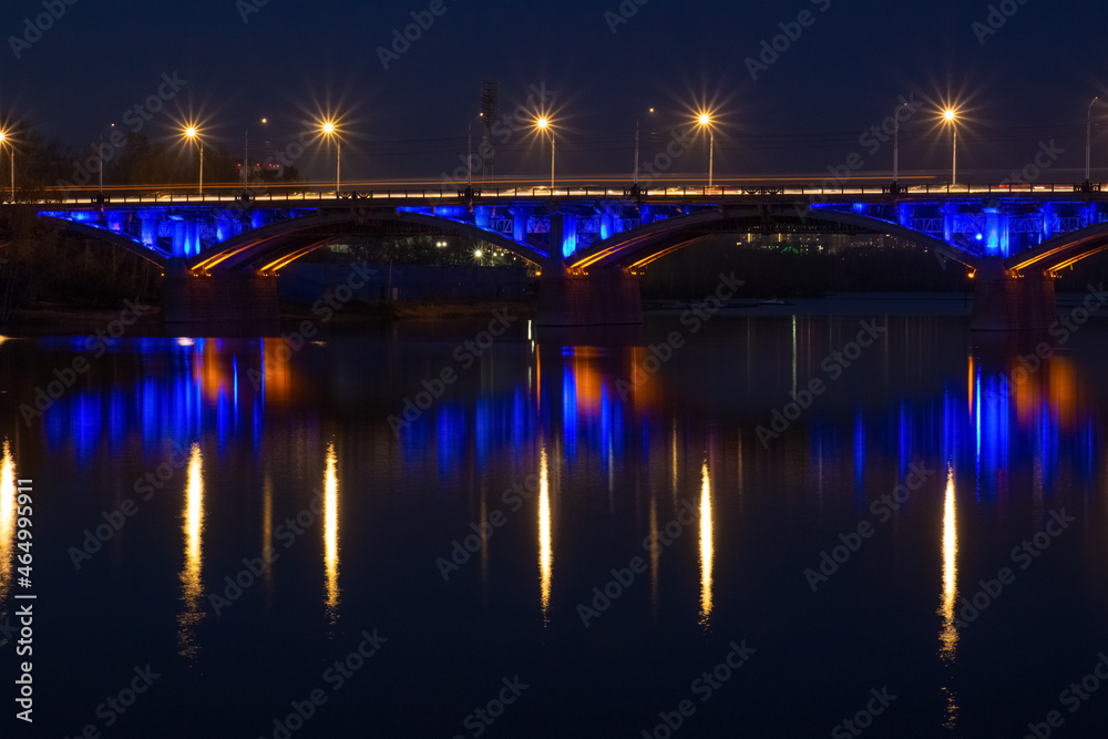 Dusk landscape with illuminated Communal bridge through Yenisei River in Krasnoyarsk, Russia. Night city lights