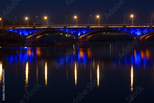 Dusk landscape with illuminated Communal bridge through Yenisei River in Krasnoyarsk, Russia. Night city lights