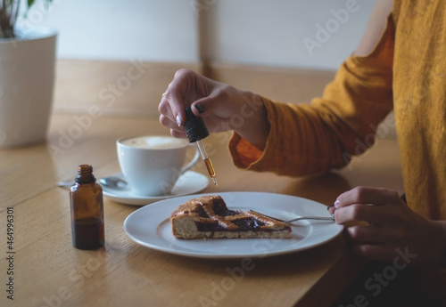 A girl in a yellow jacket is having breakfast in a cafe. Women's hands add THC and CBD oil to cherry pie. The concept of using medical marijuana.