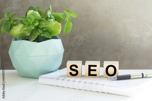 SEO words on wooden cubes on the table next to a notepad pen, potted plant