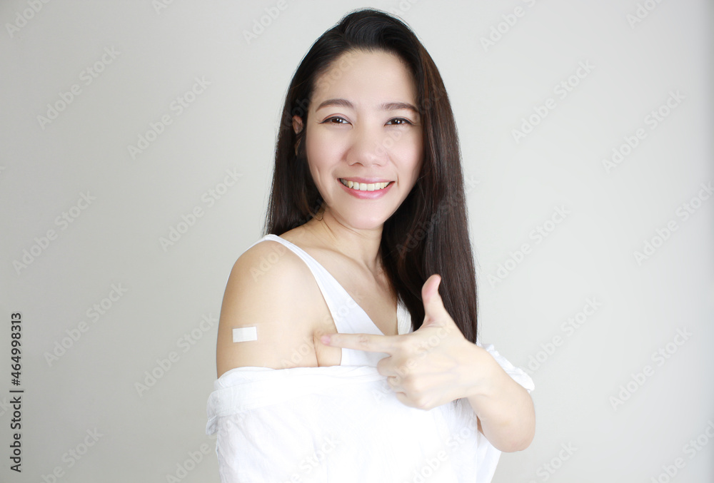 Asian happy smile beautiful women wear white shirt receive covid-19 anti virus vaccine and indicate finger on a white bandage with white background Asian happy smile beautiful women wear white shirt receive covid-19 anti virus vaccine and indicate finger on a white bandage with white background