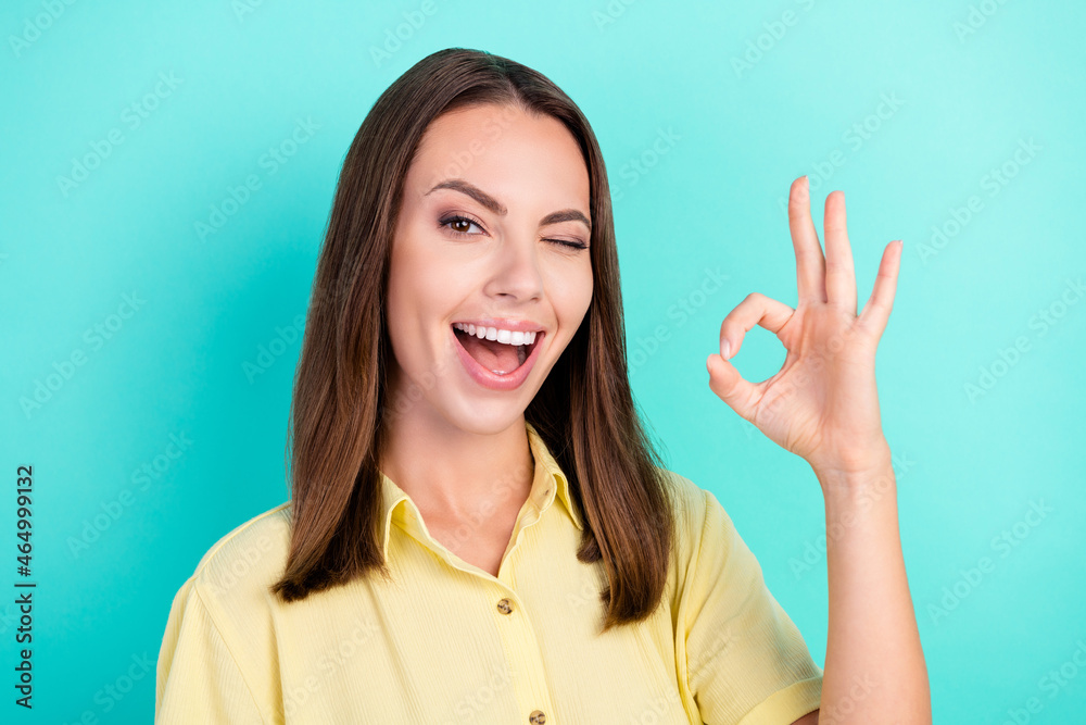 Photo of impressed millennial brunette lady show okey sign blink wear yellow blouse isolated on teal color background Photo of impressed millennial brunette lady show okey sign blink wear yellow blouse isolated on teal color background