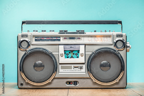 Retro outdated portable cassette tape recorder from 80s on wooden table front mint blue wall background. Vintage old style filtered photo