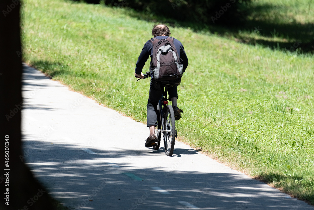 Man on bike rides bike lane through park, sunny day outdoors.