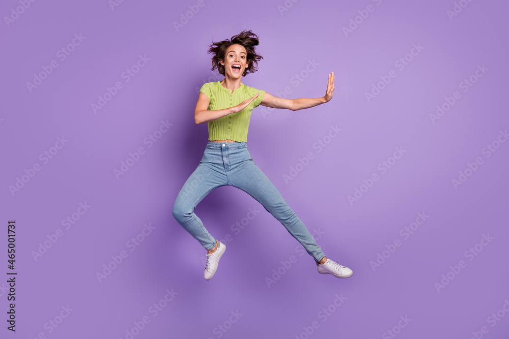 Photo of strong funky young woman dressed green t-shirt practicing karate jumping high isolated purple color background
