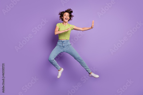Photo of strong funky young woman dressed green t-shirt practicing karate jumping high isolated purple color background