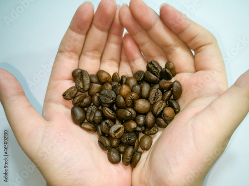 Medium roasted coffee beans, heart shape, on both palms, white background.