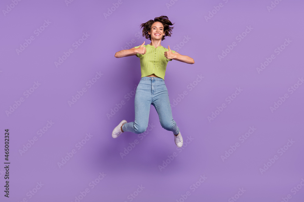 Photo of excited pretty young lady wear green t-shirt smiling jumping showing thumbs up isolated violet color background