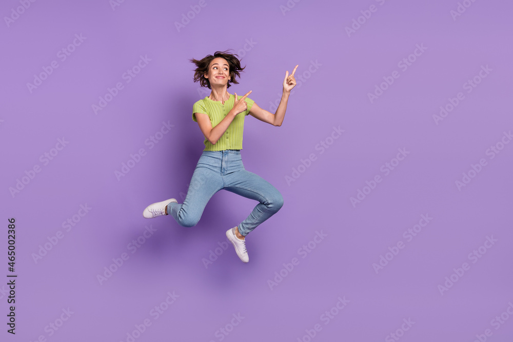 Photo of dreamy charming young woman dressed green t-shirt jumping looking pointing fingers empty space isolated purple color background