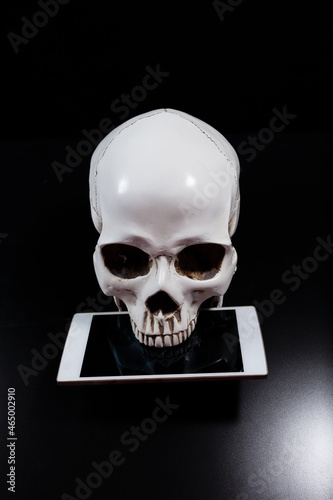 Human skull holding smartphone with cracked screen in teeth on dark background