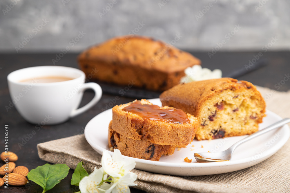 Homemade cake with raisins, almonds, soft caramel and a cup of coffee on a black concrete background. Side view, selective focus.