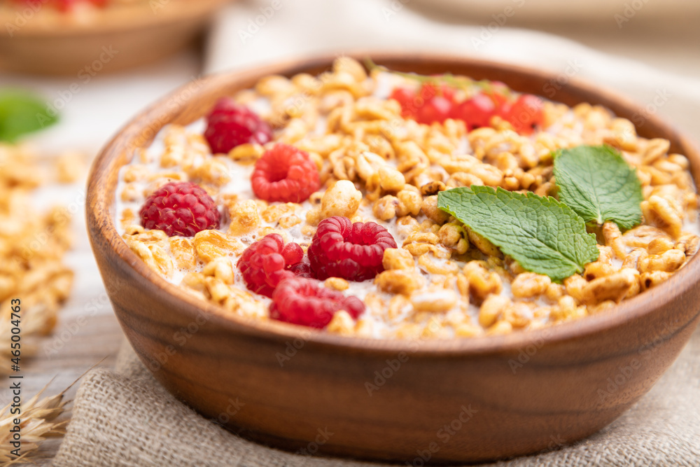 Wheat flakes porridge with milk, raspberry and currant in wooden bowl on white wooden background. Side view, selective focus. Wheat flakes porridge with milk, raspberry and currant in wooden bowl on white wooden background. Side view, selective focus.
