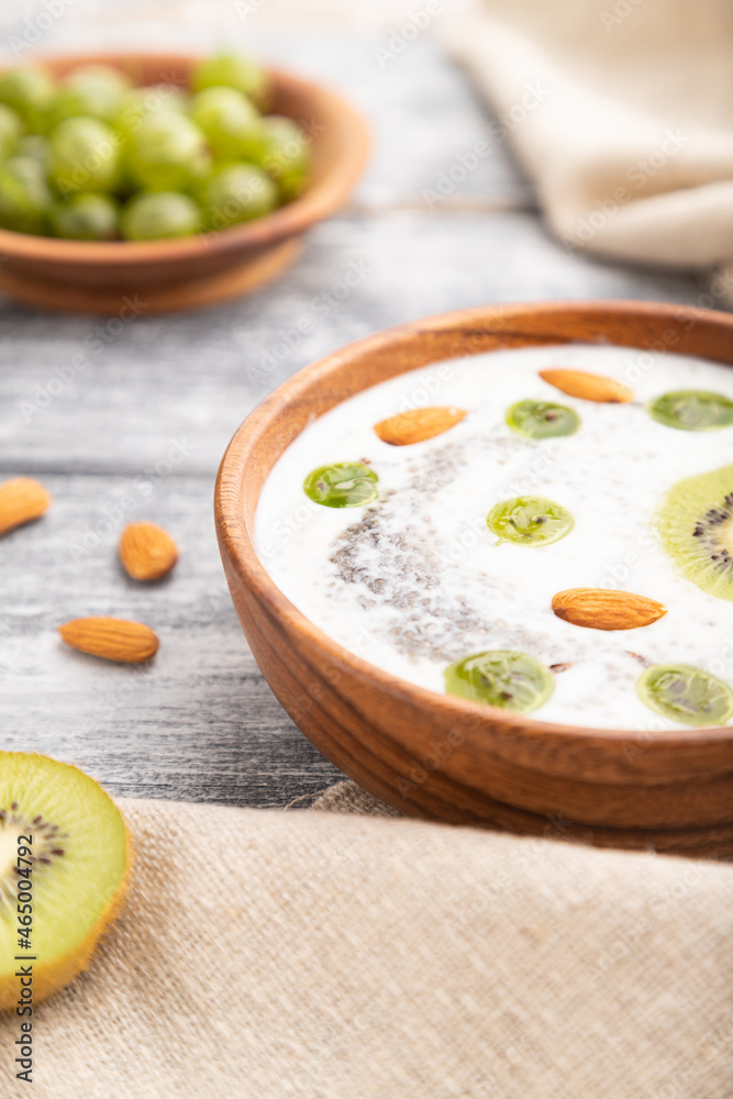 Yogurt with kiwi, gooseberry, chia and almonds in wooden bowl on gray wooden background. Side view, close up, selective focus. Yogurt with kiwi, gooseberry, chia and almonds in wooden bowl on gray wooden background. Side view, close up, selective focus.
