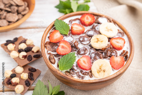 Chocolate cornflakes with milk and strawberry in wooden bowl on white wooden background. Side view, selective focus.