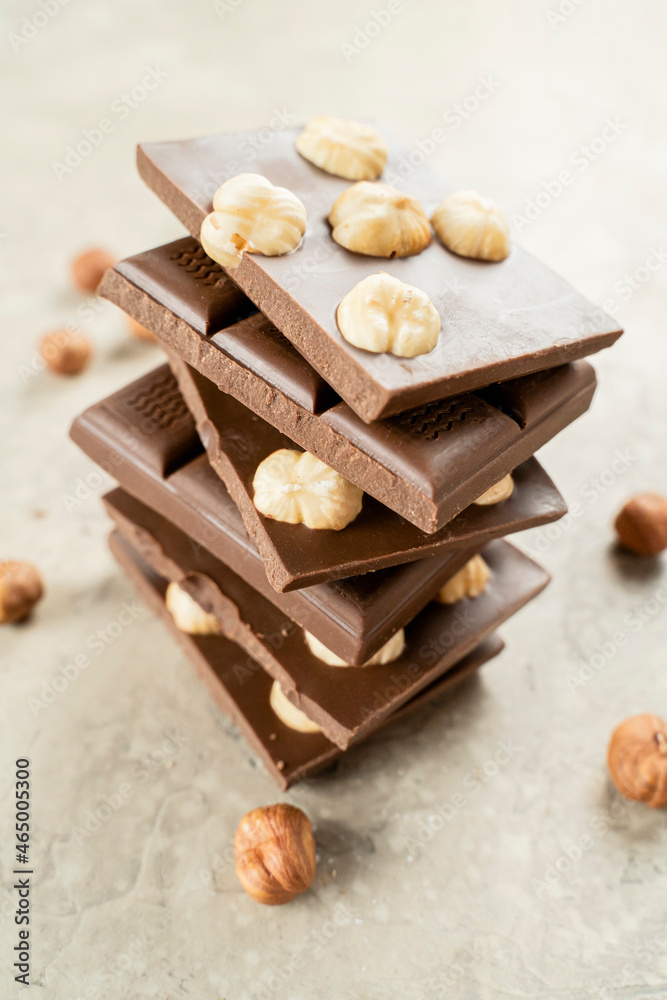 Fototapeta premium Tower of chocolate pieces with hazelnuts on a white background. Milk chocolate with nuts. Confectionery craft on table stack for Delicious Chocolate