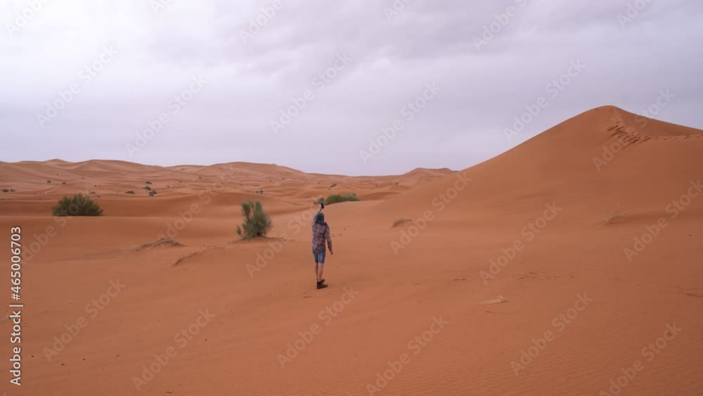 A young man in casual clothes lost in the wild Sahara trying to catch signal on the phone A young man in casual clothes lost in the wild Sahara trying to catch signal on the phone