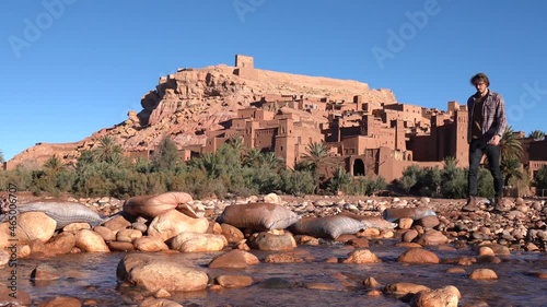 A Man Crosses on Stepping Stones the River Facing the Ait Benhaddou In Morocco - Static photo