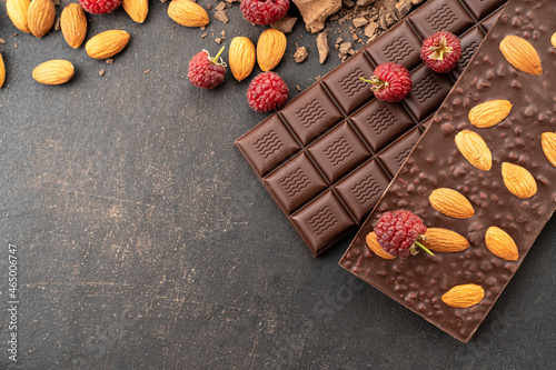 Cooking chocolate bars with almonds, raspberries, handmade sweets. Composition of bars and pieces of dark almond chocolate, raspberries on a black background, top view. Pastry craft on the table