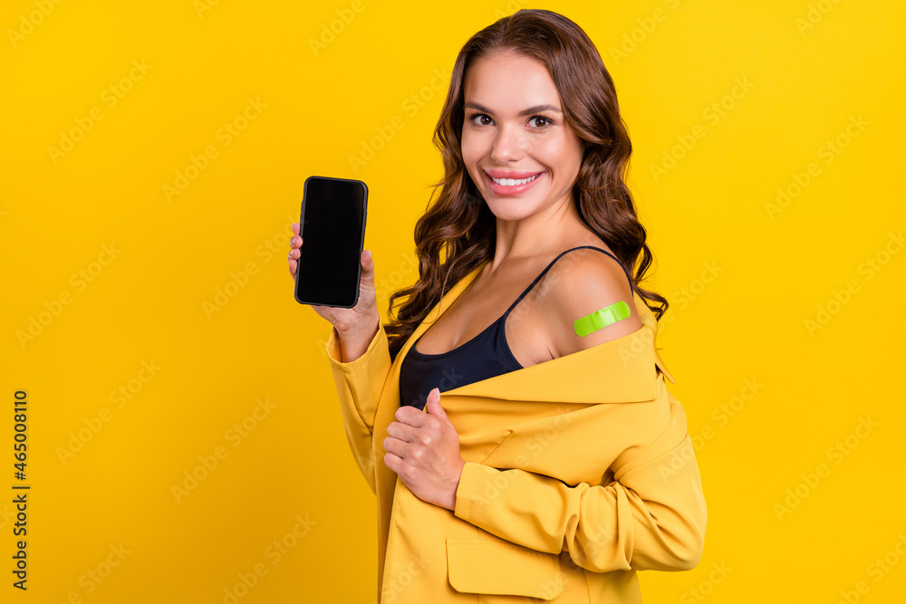 Photo of shiny attractive young woman dressed suit blazer holding device empty space sticky plaster shoulder isolated yellow color background Photo of shiny attractive young woman dressed suit blazer holding device empty space sticky plaster shoulder isolated yellow color background