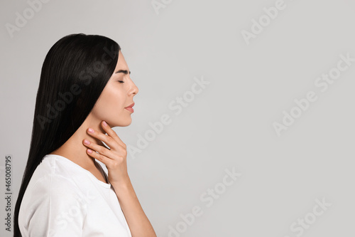 Young woman doing thyroid self examination on light background. Space for text