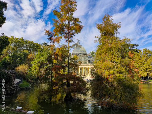 The Crystal Palace in Madrid's Retiro Park with an autumnal landscape and a somewhat cloudy day at sunset. Trees with fall colors and autumn light. 