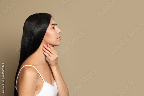 Young woman doing thyroid self examination on beige background. Space for text photo