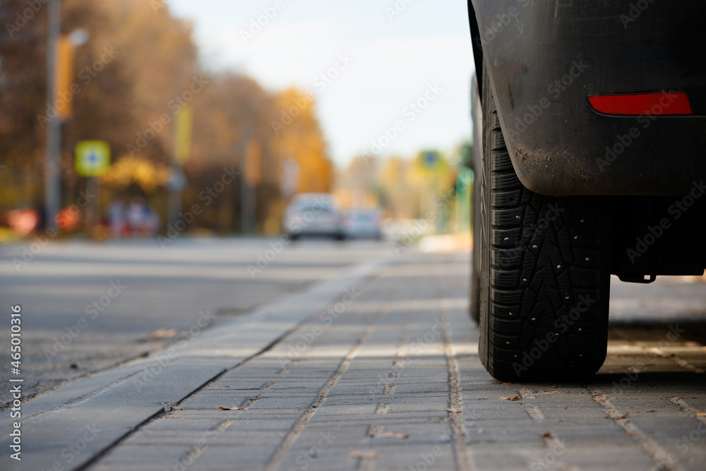 A car with winter studded wheels standing on the side of the road against the background of passing cars and bright colors of autumn. Preparing for the winter season, the first frost and snow