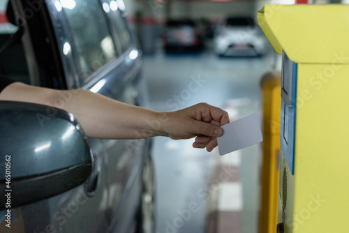 Caucasian woman driving her car approaches her hand with white security card to access the parking lot to the control machine and open the barriers.
