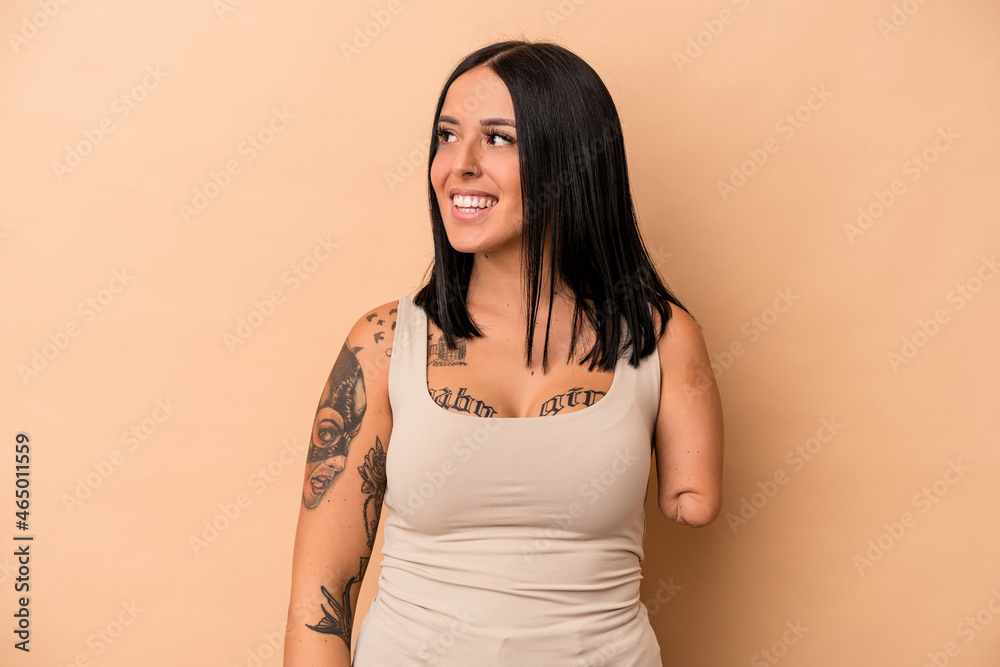 Young caucasian woman with one arm isolated on beige background looks aside smiling, cheerful and pleasant. Young caucasian woman with one arm isolated on beige background looks aside smiling, cheerful and pleasant.