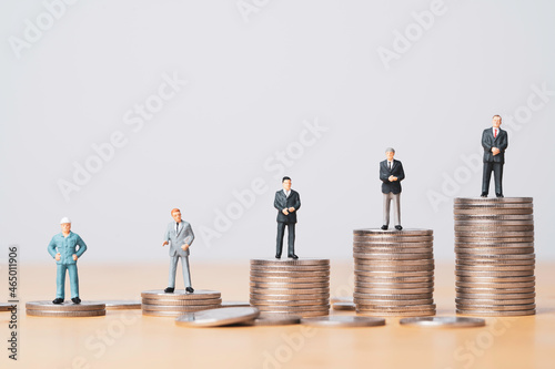 Fotografiet Different miniature businessman standing on different height coins stacking , Inequality income and salary in each position in company concept