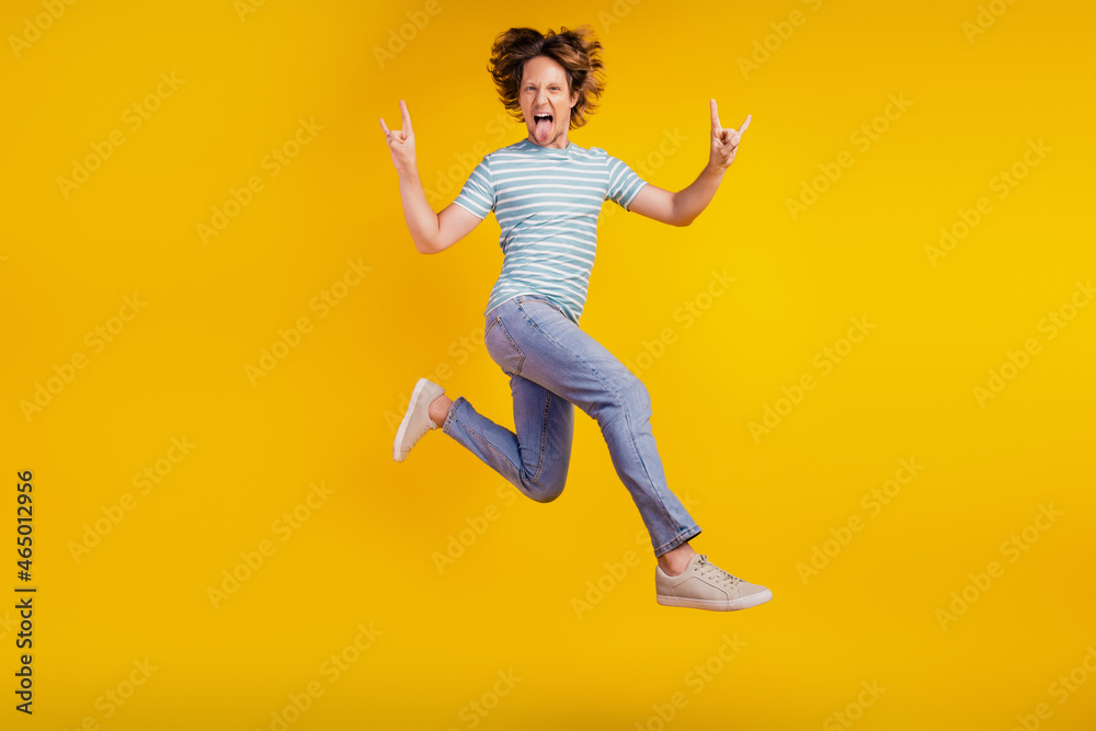 Full-body photo of young cheerful man show fingers horns rock sign jump rude isolated on shine yellow background
