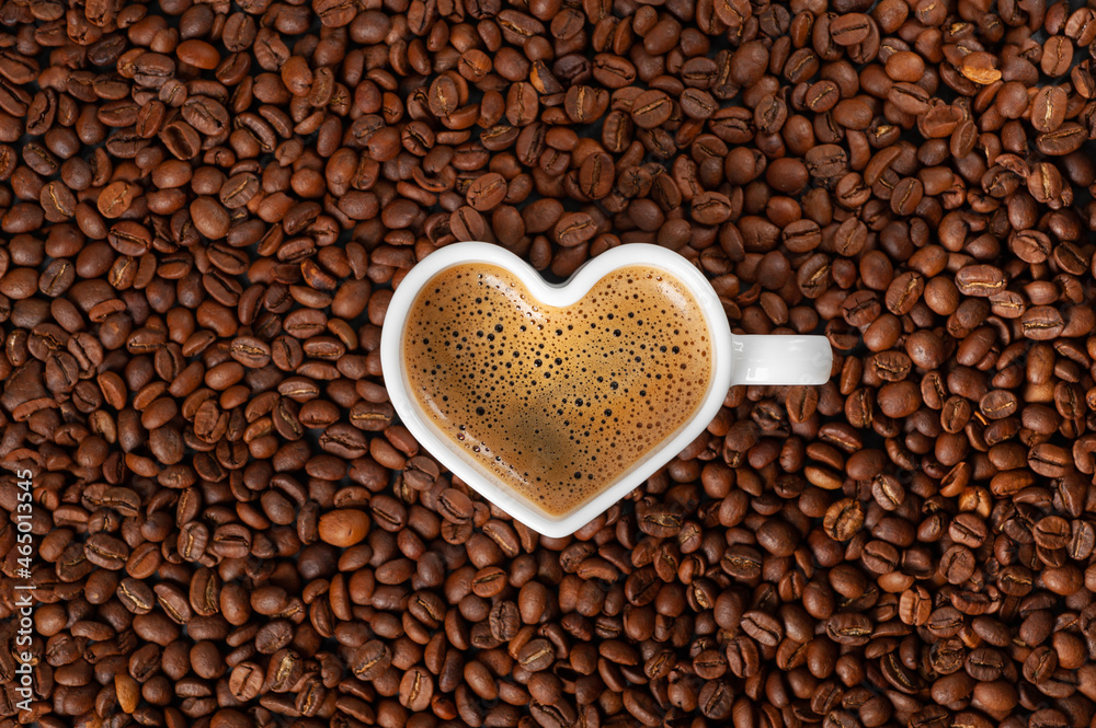 Coffee with a beautiful froth in a mug in the shape of a heart on a background of coffee beans. copy space Coffee with a beautiful froth in a mug in the shape of a heart on a background of coffee beans. copy space