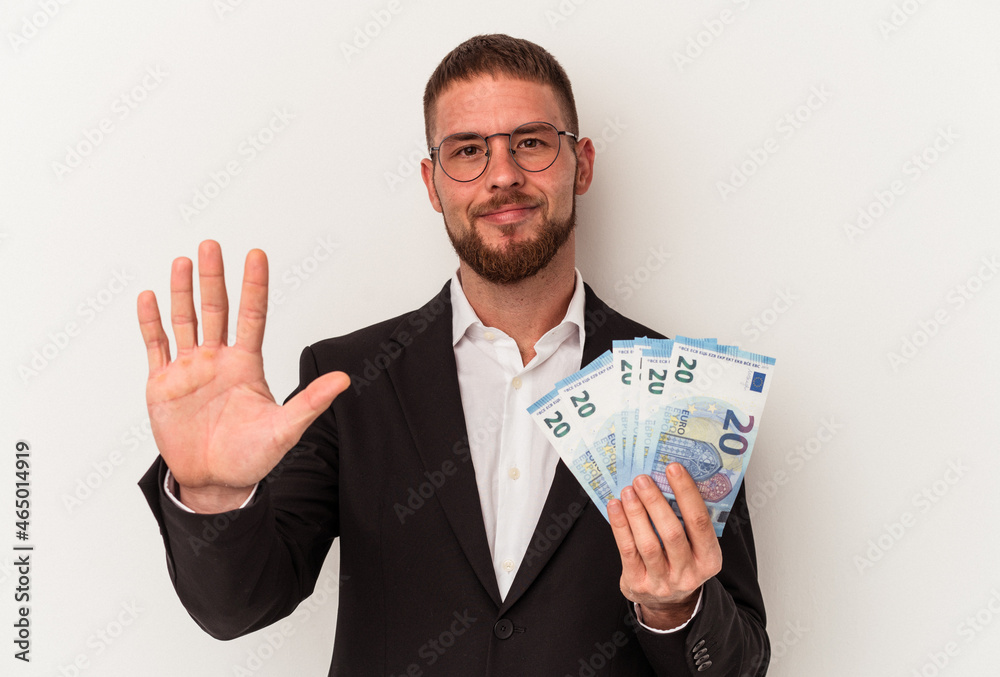 Young business caucasian man holding banknotes isolated on white background smiling cheerful showing number five with fingers. Young business caucasian man holding banknotes isolated on white background smiling cheerful showing number five with fingers.