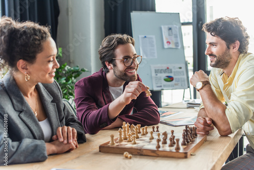 Positive interracial business people playing chess in office