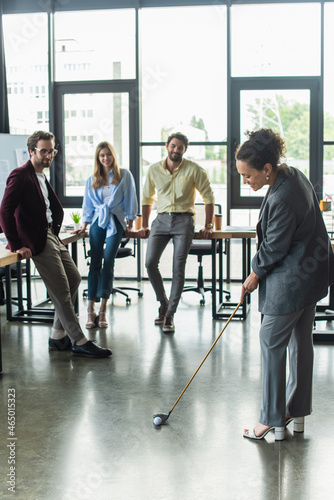 African american businesswoman playing golf near colleagues in office