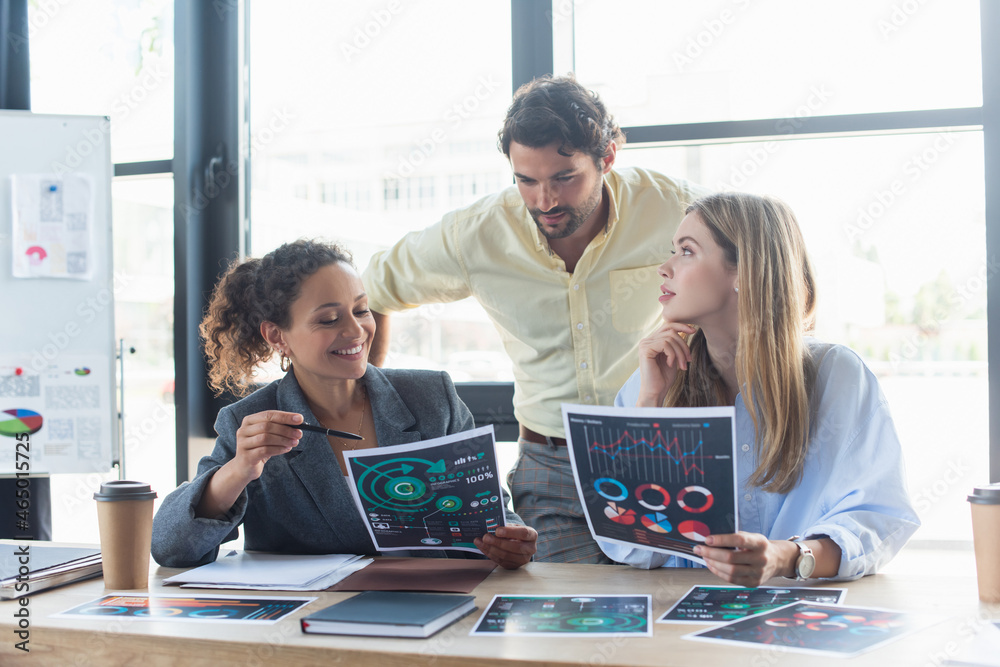 Smiling african american businesswoman pointing at document near colleagues and paper folder in office Smiling african american businesswoman pointing at document near colleagues and paper folder in office