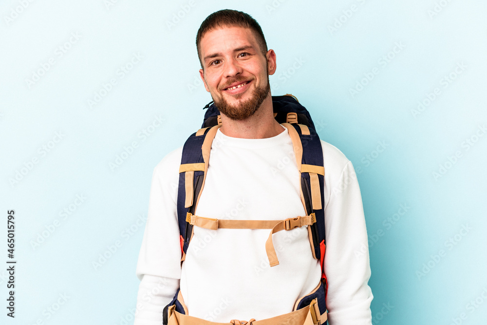 Young hiker caucasian man isolated on blue background happy, smiling and cheerful. Young hiker caucasian man isolated on blue background happy, smiling and cheerful.