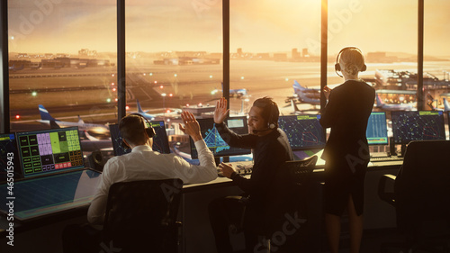 Air Traffic Control Team Working in a Modern Airport Tower at Sunset. Controllers Celebrate Sucessful Landing, Giving High Five to Each Other. Office Room is Full of Navigation Screens, Flight Radars