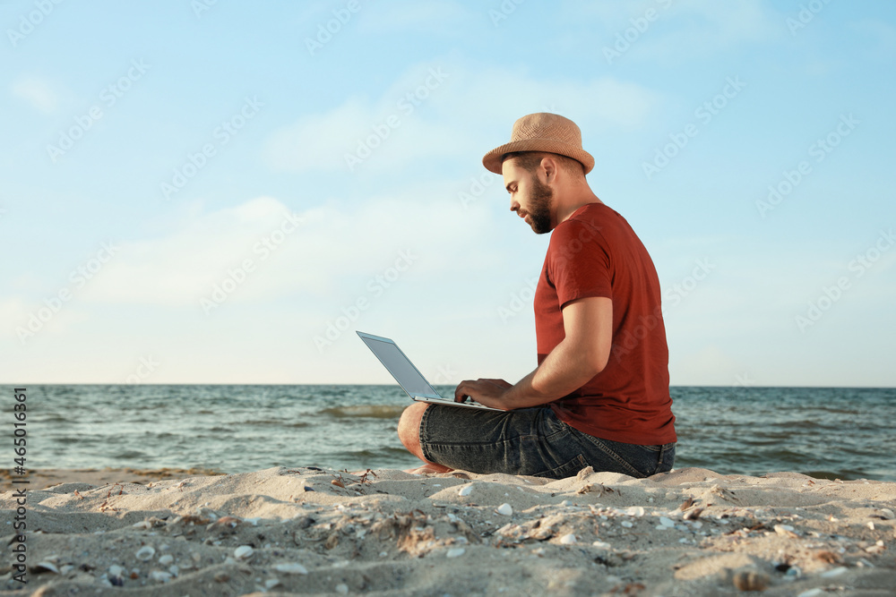 Man working with laptop on beach. Space for text