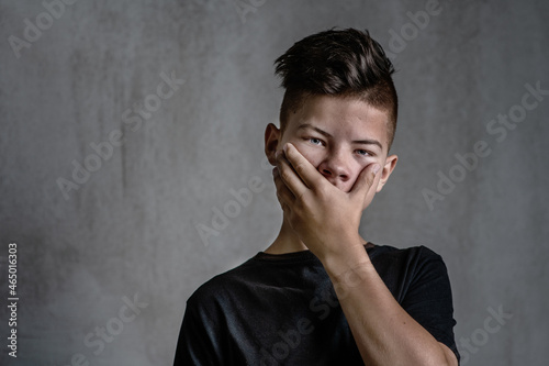 Sad teen boy covered his mouth with his hands. Problems of suppression of emotional detachment and isolation of adolescent children. Difficulties growing up during the transition period