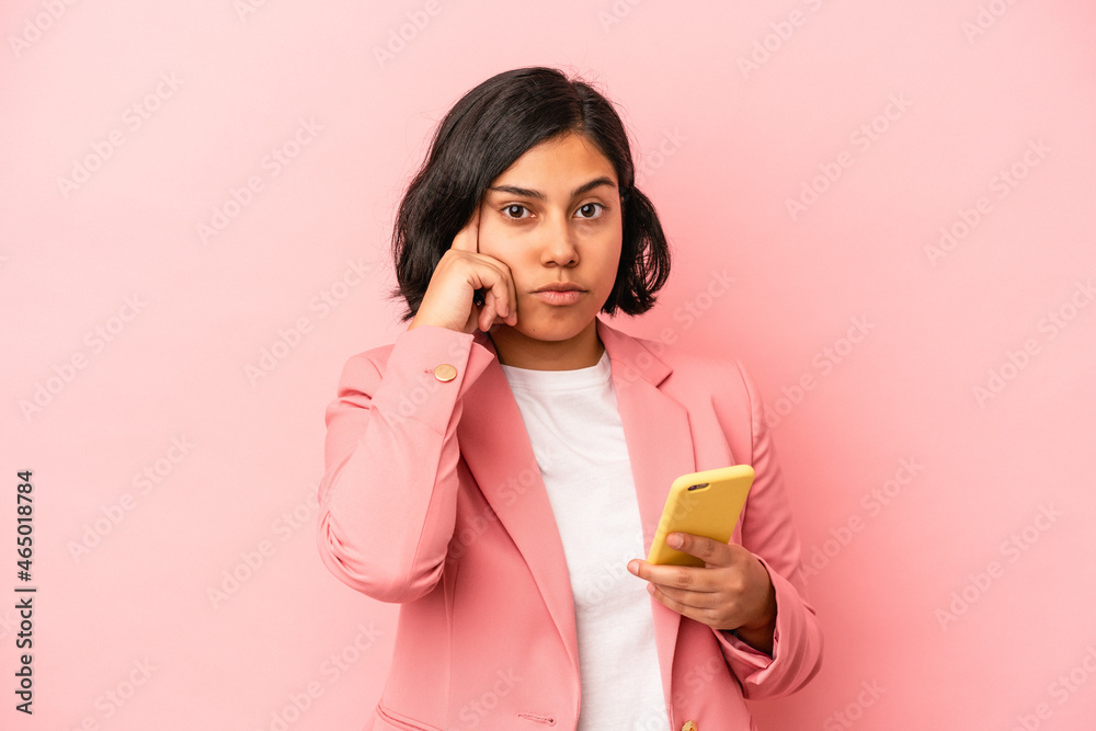 Young latin woman holding mobile phone isolated on pink background pointing temple with finger, thinking, focused on a task.