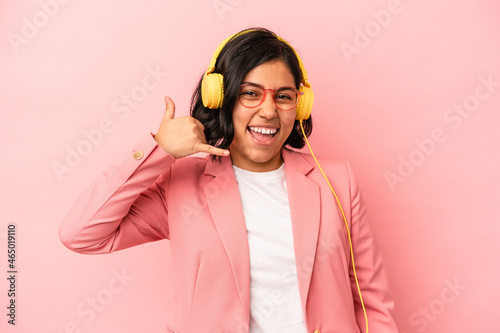 Young latin woman listening to music isolated on pink background showing a mobile phone call gesture with fingers. © Asier