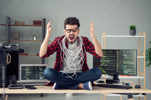 Portrait of attractive mad angry evil desperate frustrated guy hacker sitting on table yelling at work place station indoors
