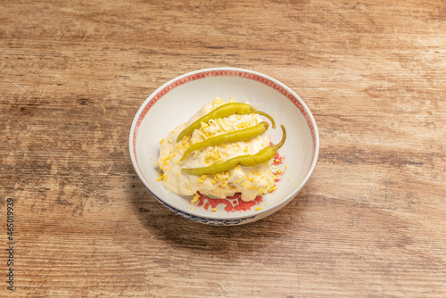 bowl with Russian salad with boiled egg, mayonnaise sauce and piparras on top